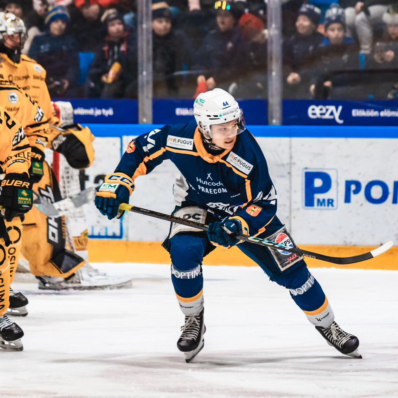 Hockey players in action on an ice rink with spectators in the background.