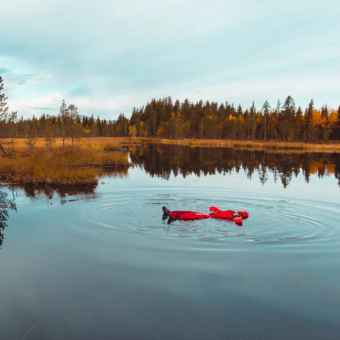 Person floating in a red rescue suit in arctic lake wilderness, safe and dry. Arctic floating in the wilderness Safartica