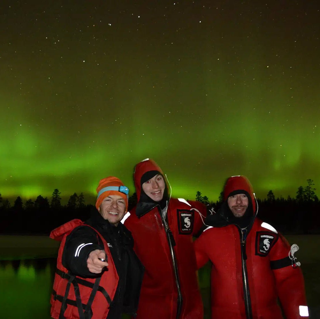 Three people in rescue suits under Northern Lights ready for Aurora Borealis floating on the lake experience by Safartica