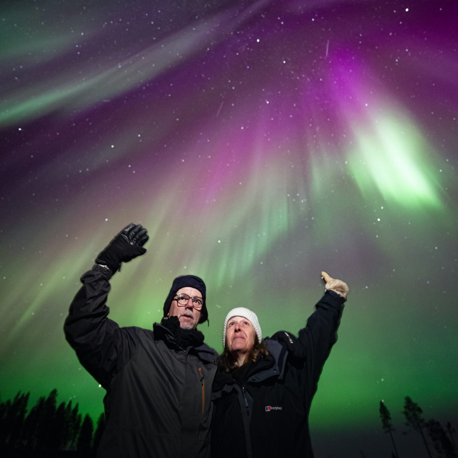 Couple admiring vibrant Northern Lights during Aurora Hunting Pro Guaranteed Tour by Book Lapland
