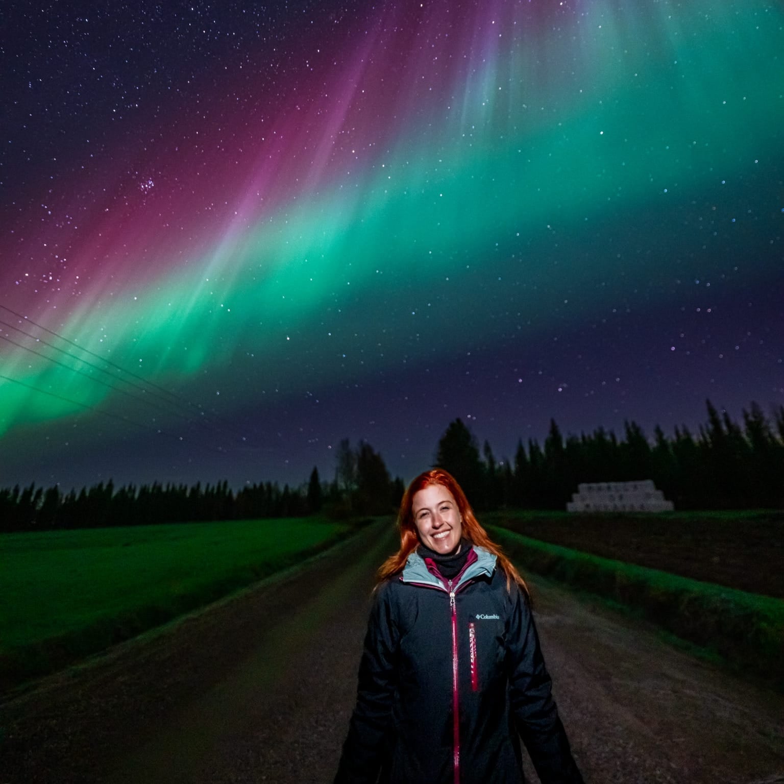 Smiling woman under vibrant Northern Lights at night on Aurora Borealis Hunting Premium Guaranteed Tour by Book Lapland