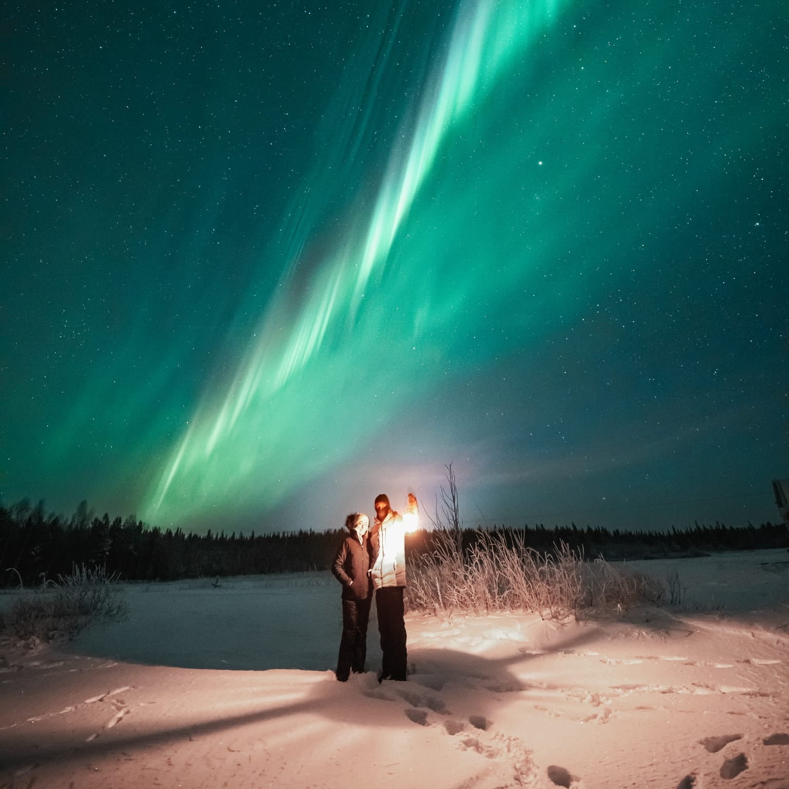 Couple under bright northern lights during Aurora Borealis Hunting Pro Guaranteed Bus Tour by Book Lapland