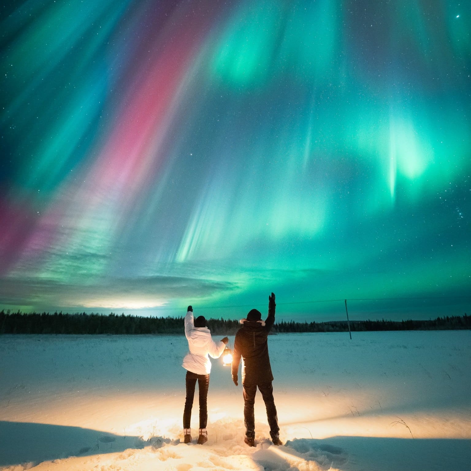 Two people watch the vibrant Northern Lights during the Aurora Borealis Hunting Medium Group Tour Guaranteed by Book Lapland