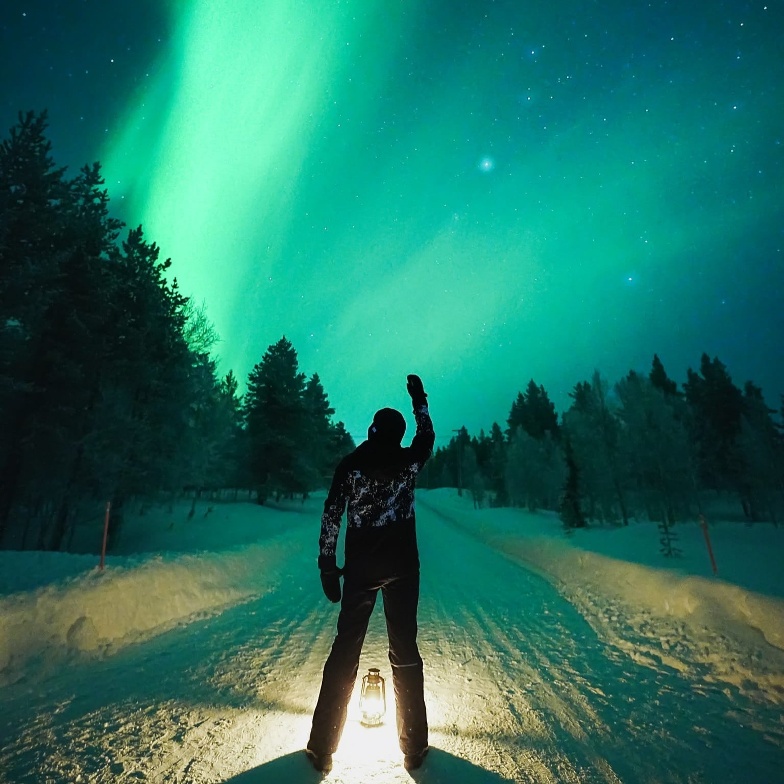 Person standing on snowy road under aurora borealis during Aurora Hunting Medium Group Tour Guaranteed by Book Lapland.