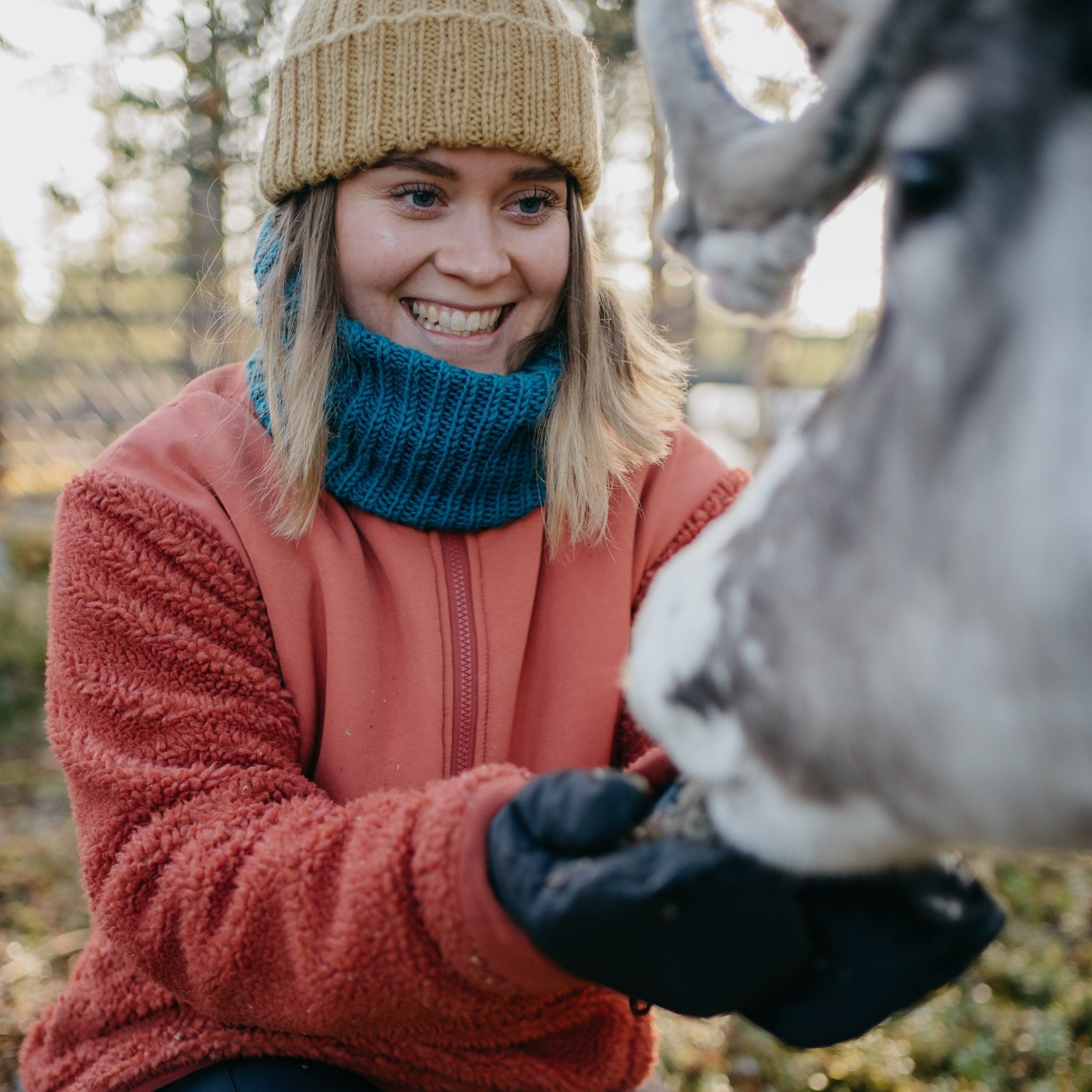 Woman smiling while feeding a reindeer during Reindeer, Berries & Fire – Experience Authentic Lapland Nature by Porovaara