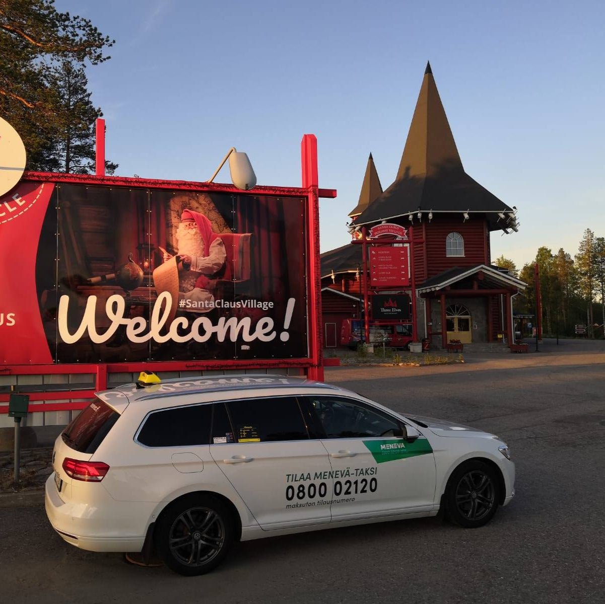 White car with green logo parked in front of a 'Welcome to Santa Claus Village' sign.
