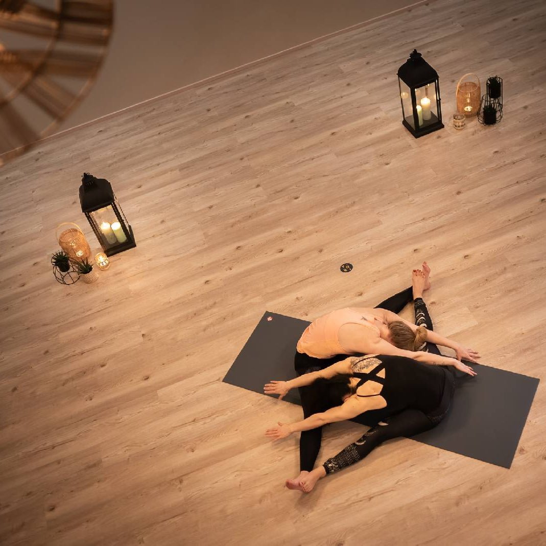 Two women practicing seated yoga stretch on mats surrounded by candles and lanterns Yogaclass Lapin Väki