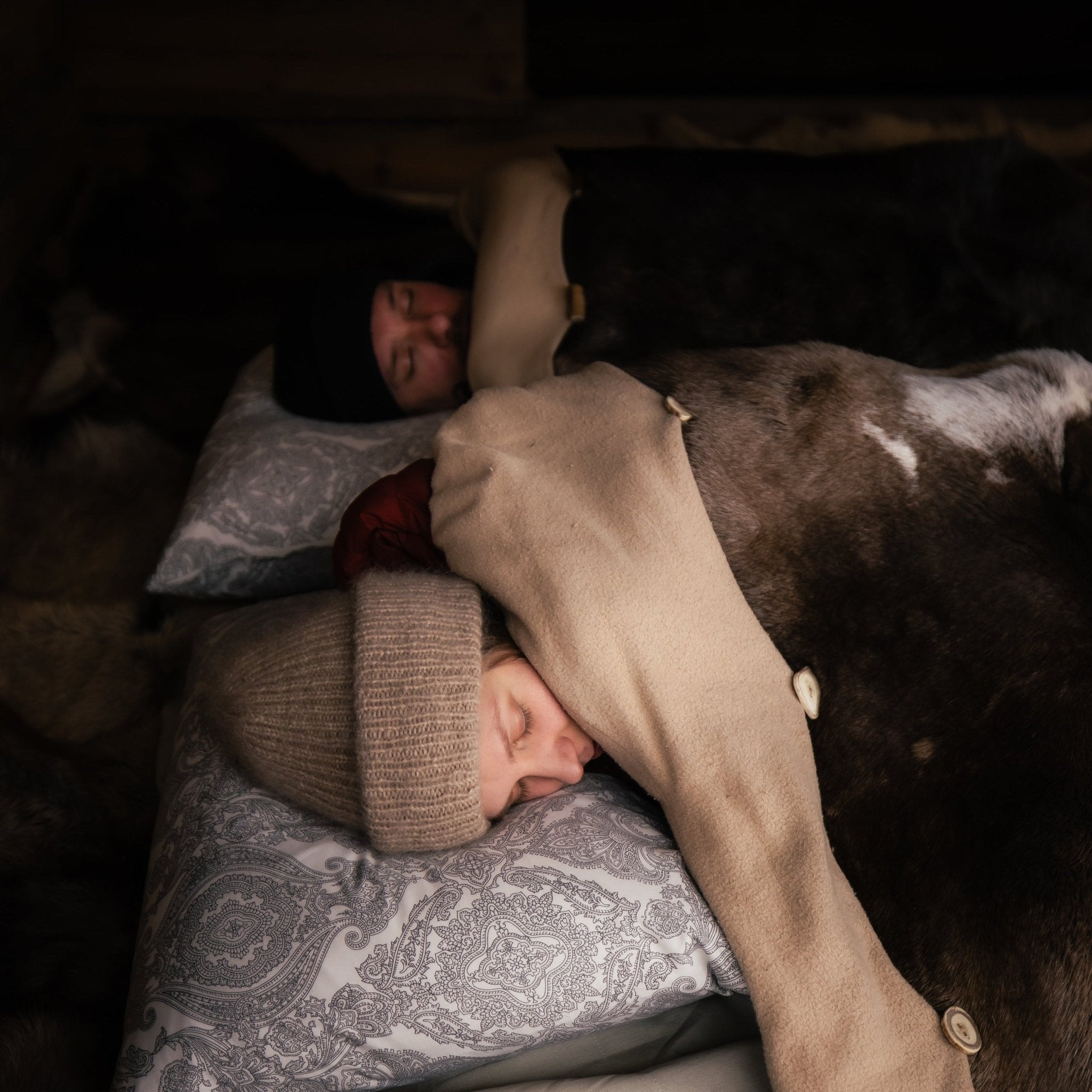 A night in the wilderness with two people sleeping warmly under a reindeer hide sleeping bag indoors.