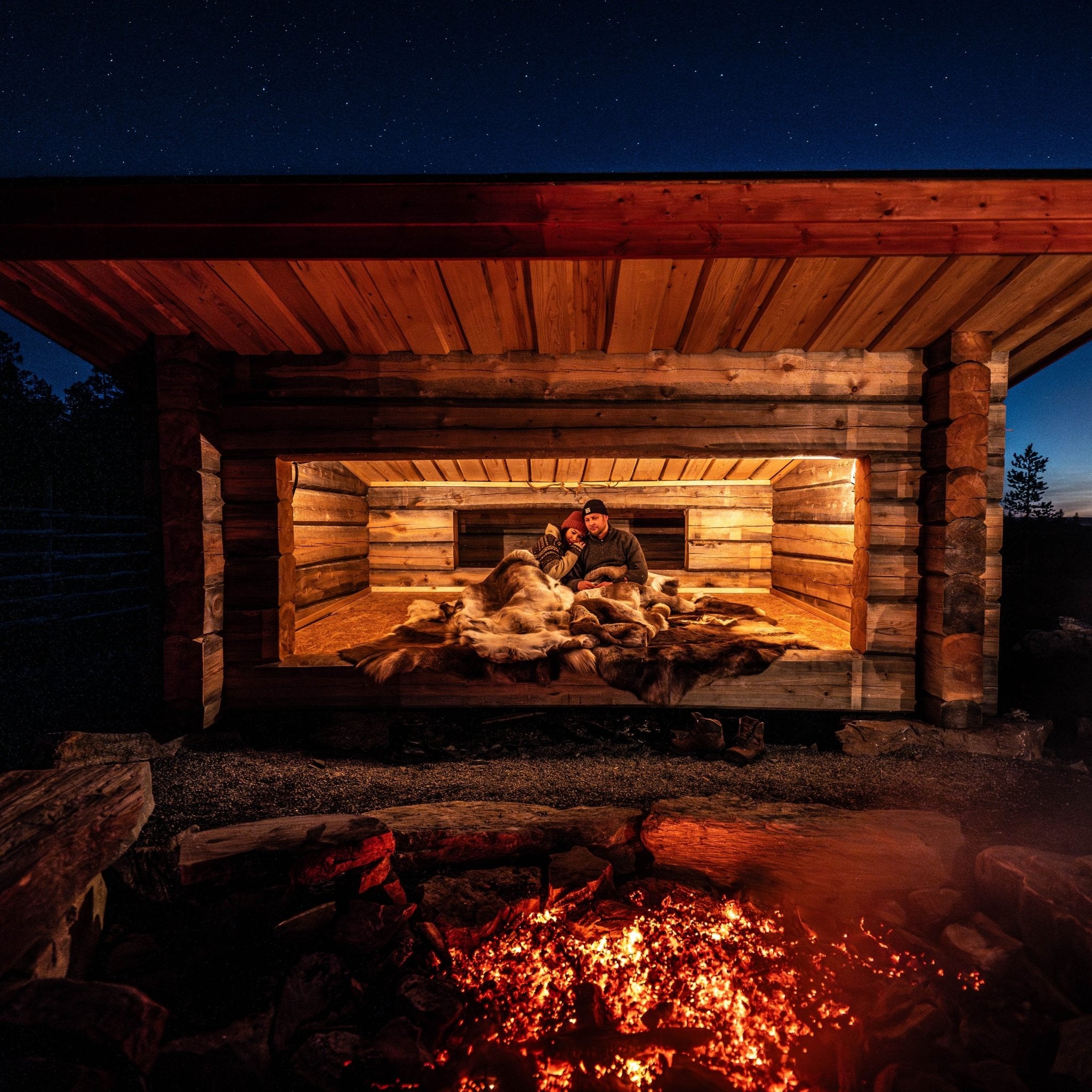A night in the wilderness with a warm reindeer hide sleeping bag in a traditional Lapland lean-to by the campfire at night.