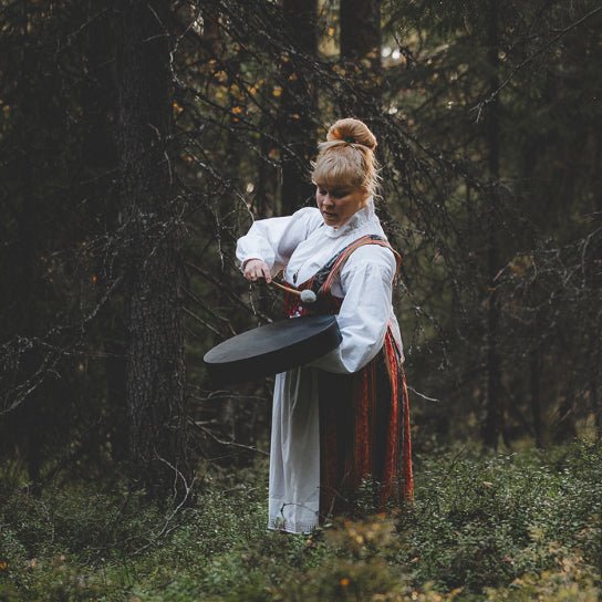 Woman in traditional Finnish dress playing a drum in forest for Stories and Songs of the Old Spirits by Lapin Väki