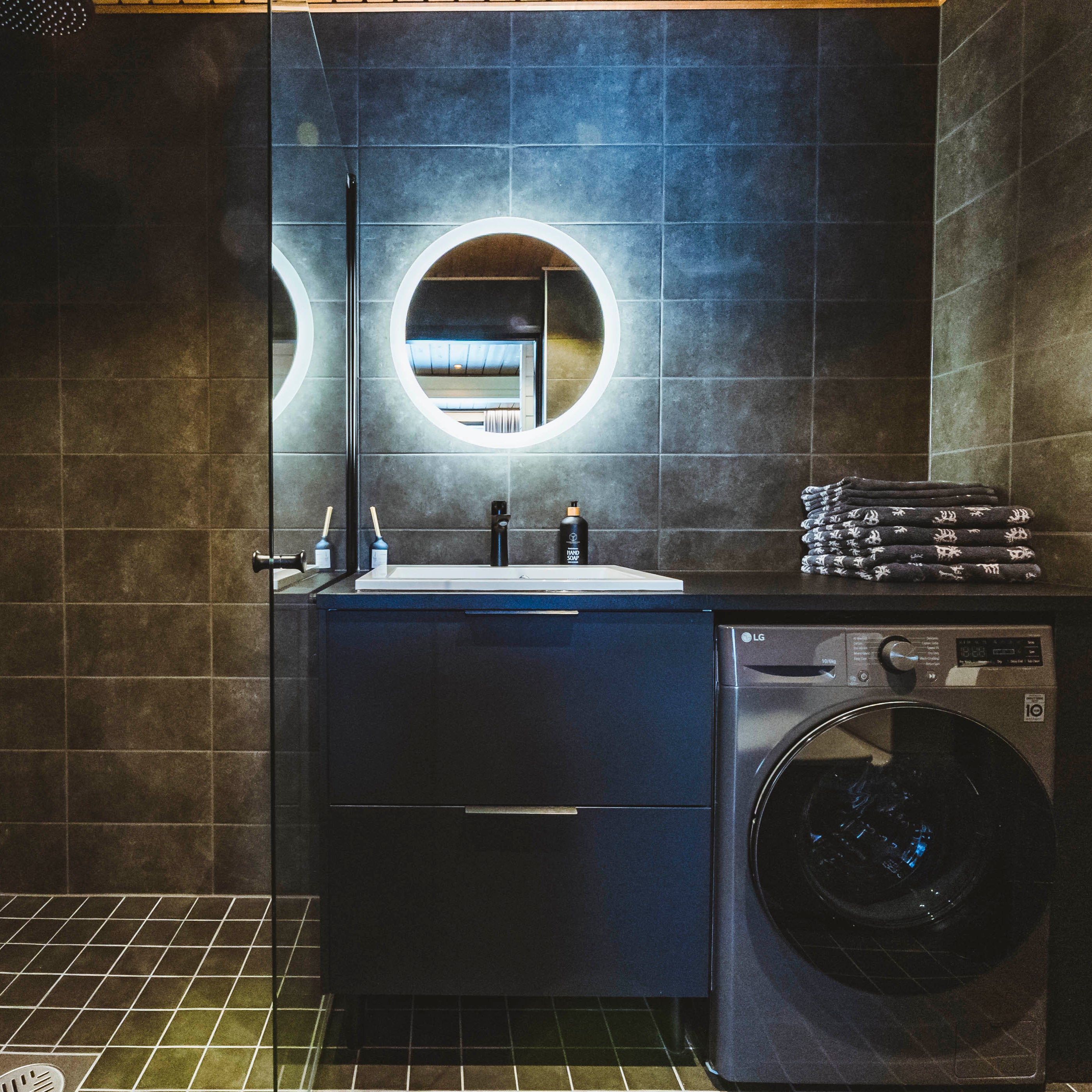 Modern bathroom with illuminated round mirror and washing machine in the Most unique sleeping experience in Lapland by Your City Guide