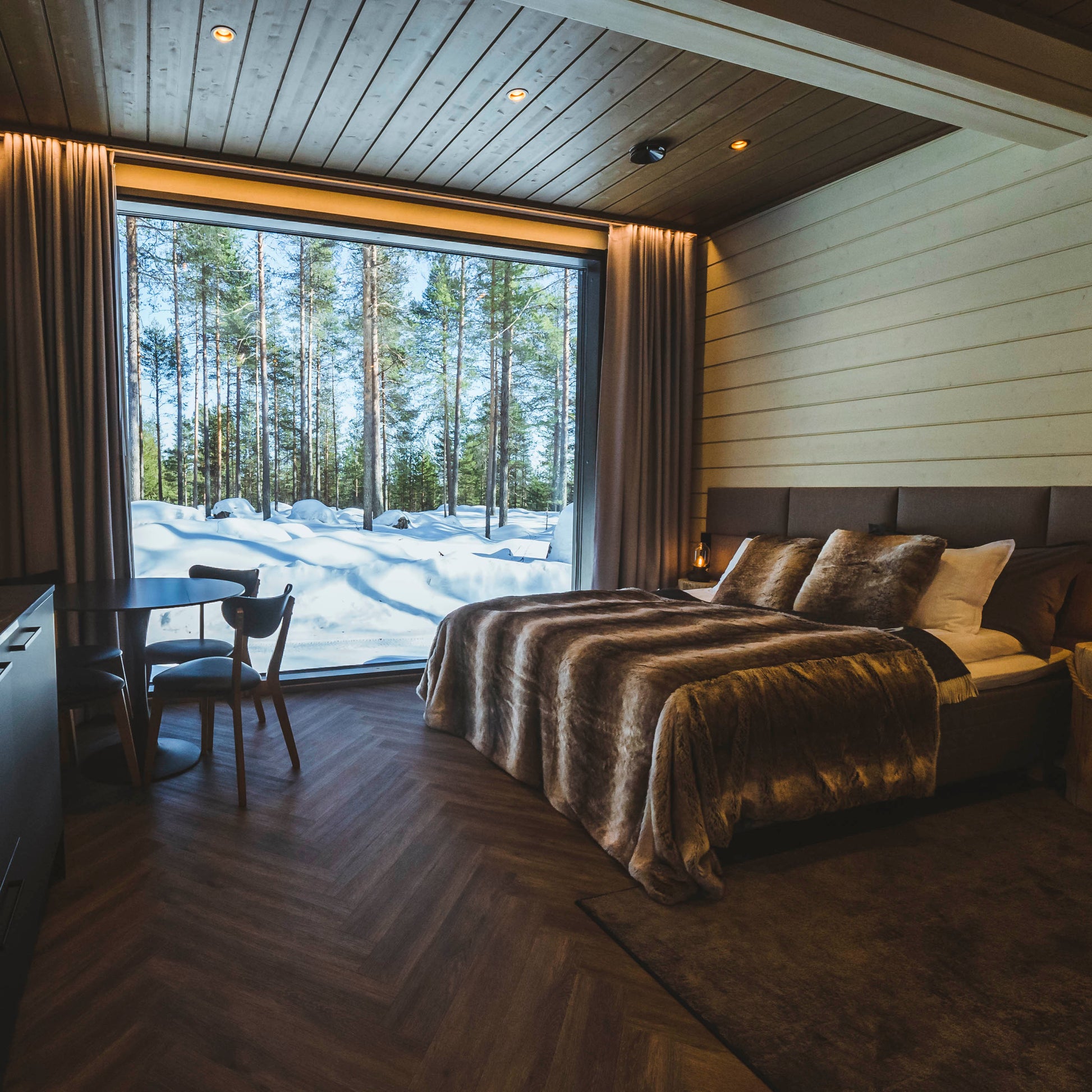 Cozy bedroom with large window showing snowy Arctic forest, perfect for Most unique sleeping experience in Lapland by Your City Guide.