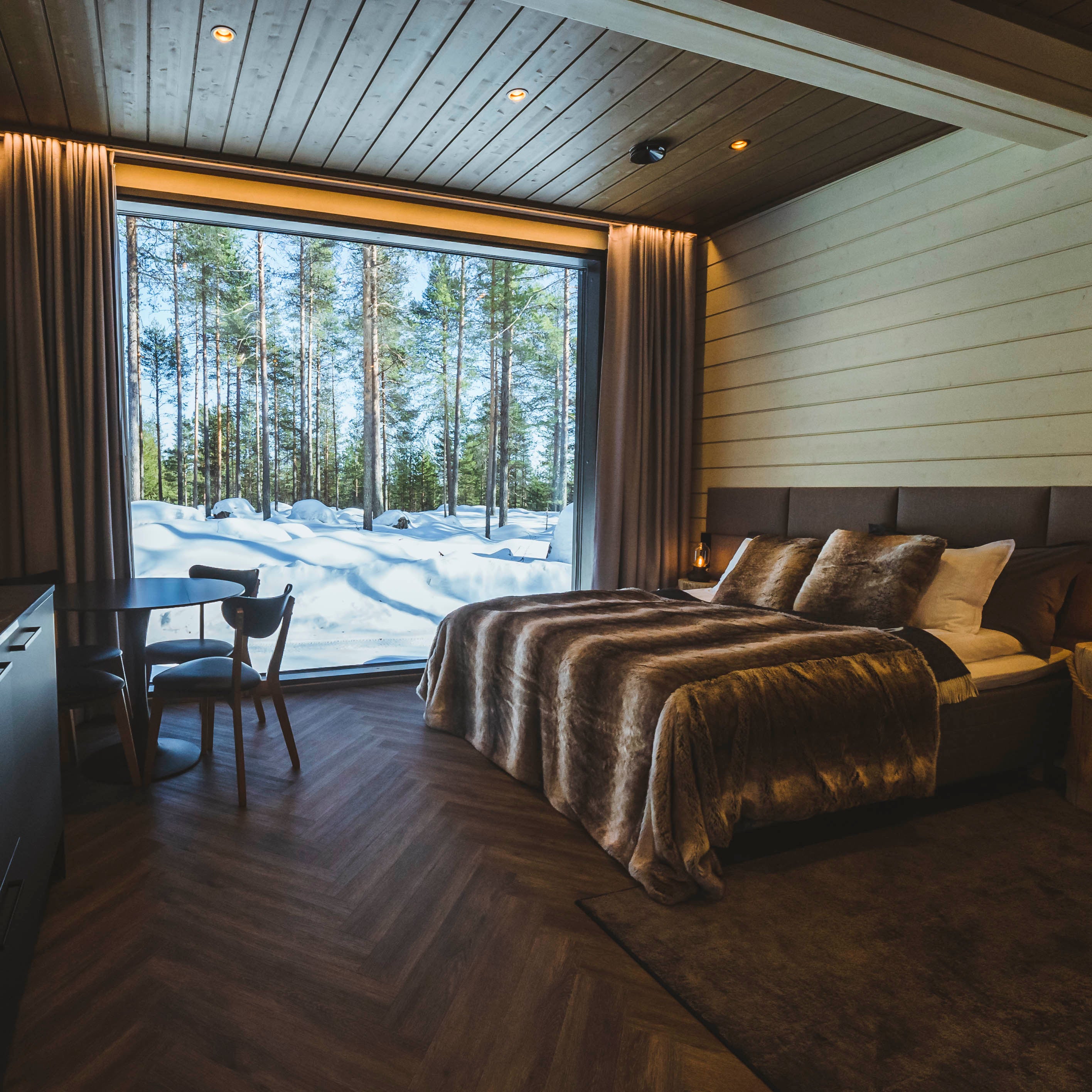 Cozy bedroom with large window showing snowy Arctic forest, perfect for Most unique sleeping experience in Lapland by Your City Guide.