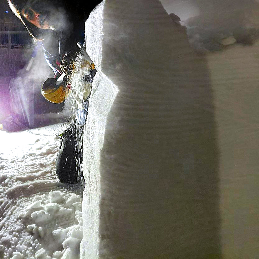 Person cleaning a car with a snow brush on a snowy street at night.