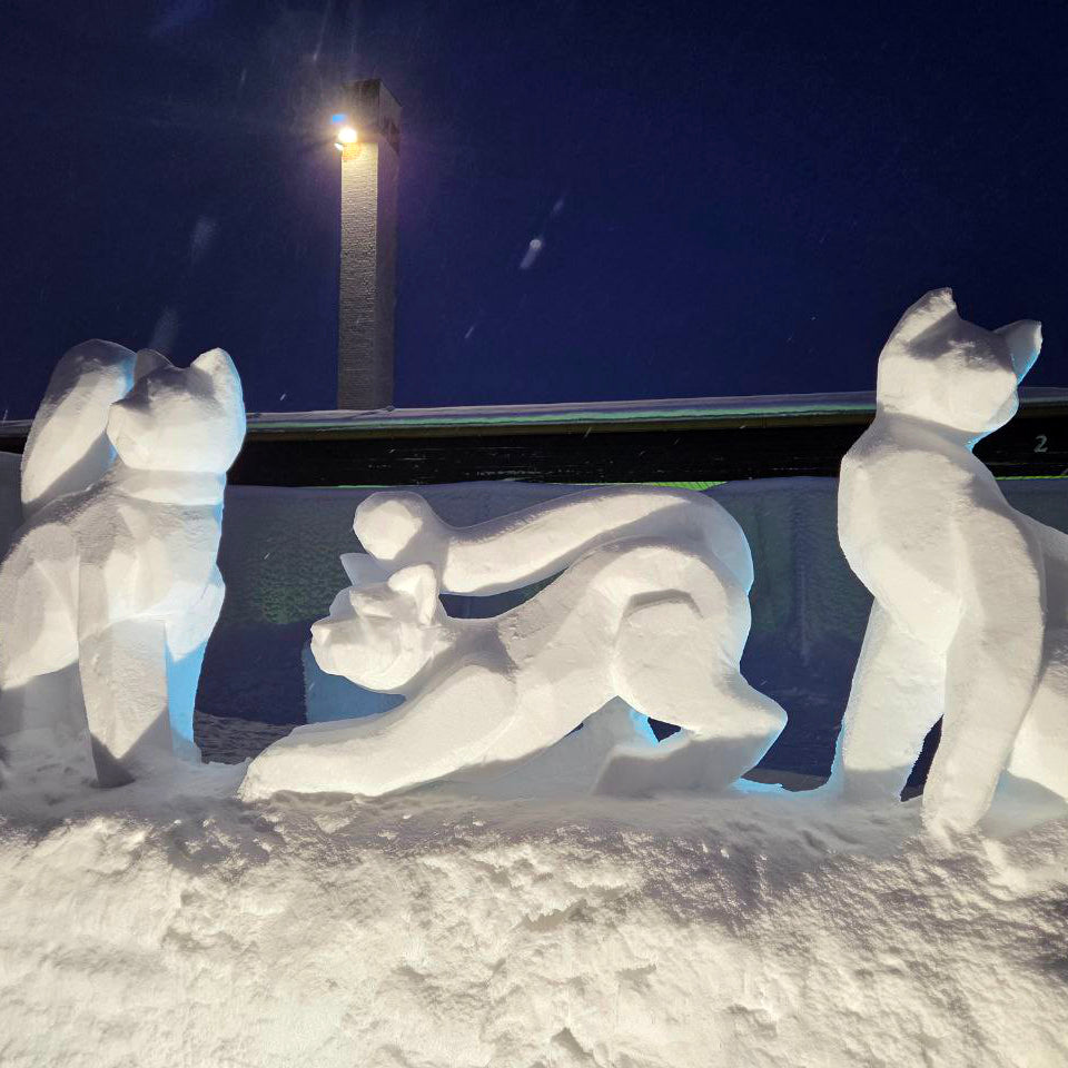 Snow sculpture of three animals in front of a lighthouse at night