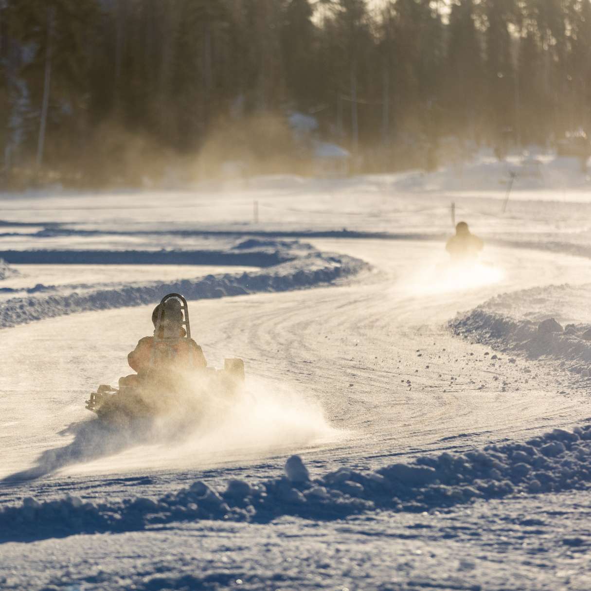 Two snowmobiles racing on a snowy track with trees in the background