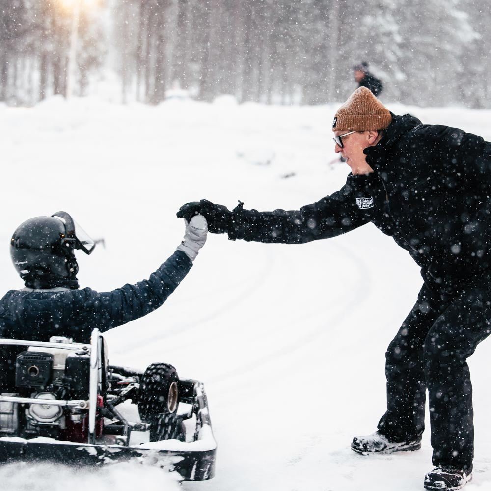 Two people in winter gear shaking hands in a snowy landscape with a snowmobile.