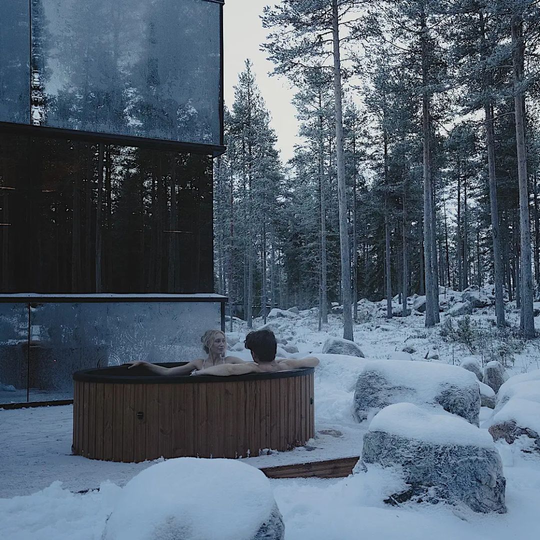 Couple relaxing in outdoor hot tub surrounded by snow at Arctic spa experience with bathrobe dinner by Invisible forest lodge