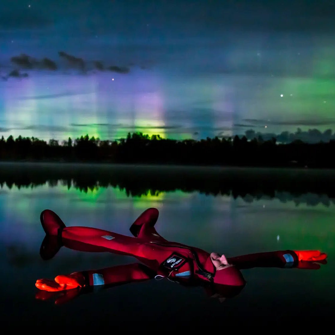 Person floating on a frozen lake under Northern Lights in a rescue suit Aurora Borealis floating on the lake Safartica