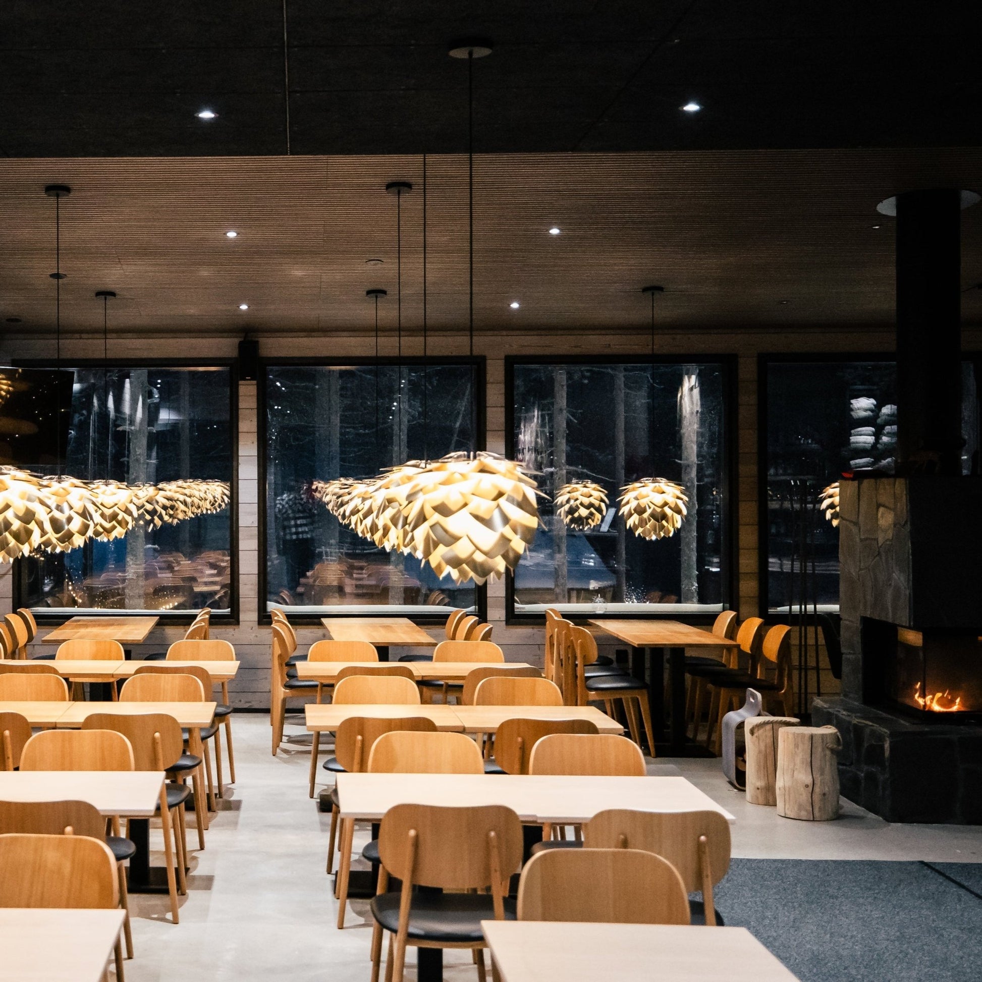 Modern restaurant interior with wooden tables, chairs, and decorative ceiling lights.