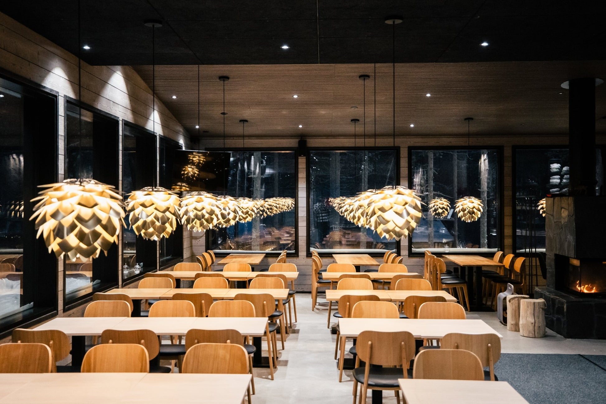 Cozy dining area with wooden tables, pendant lights, and fireplace at Lapland Winter Park - Snow experiences - Vendor
