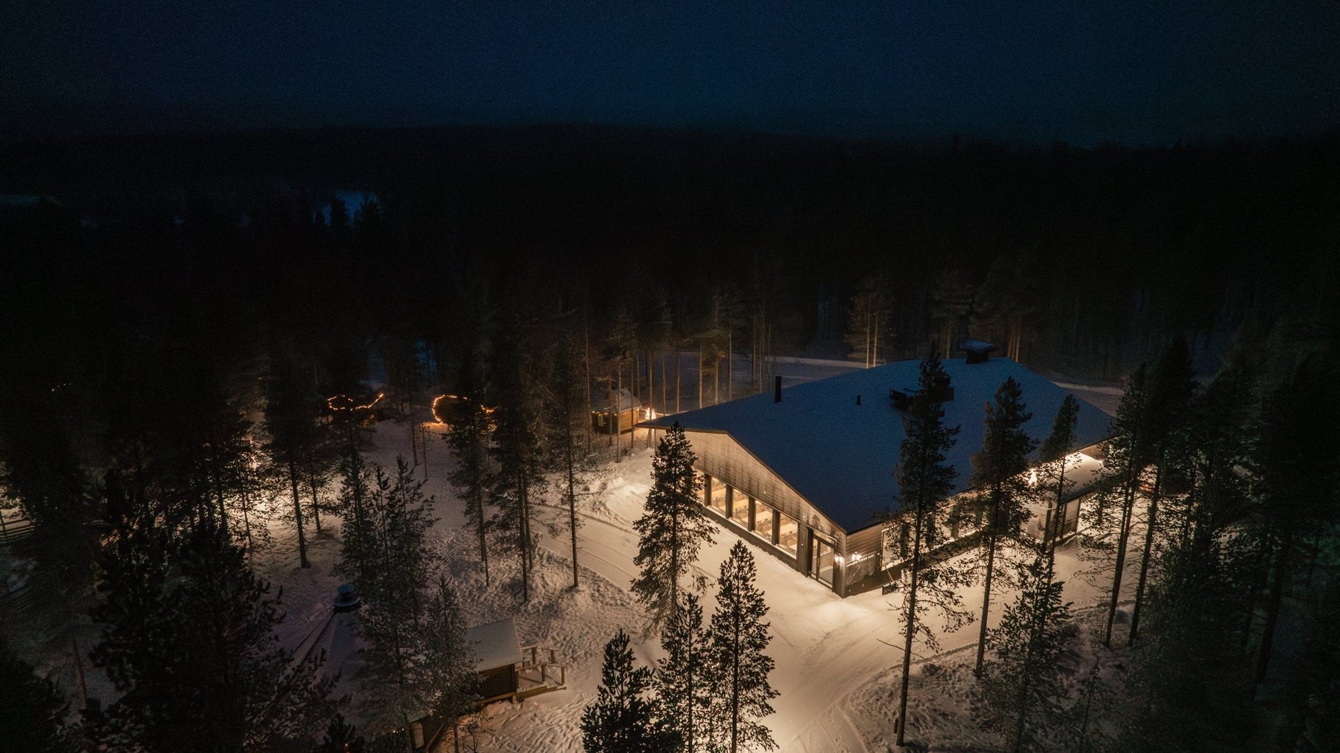 Night view of snow-covered Lapland Winter Park surrounded by trees with warmly lit cabin - Lapland Winter Park - Snow experiences