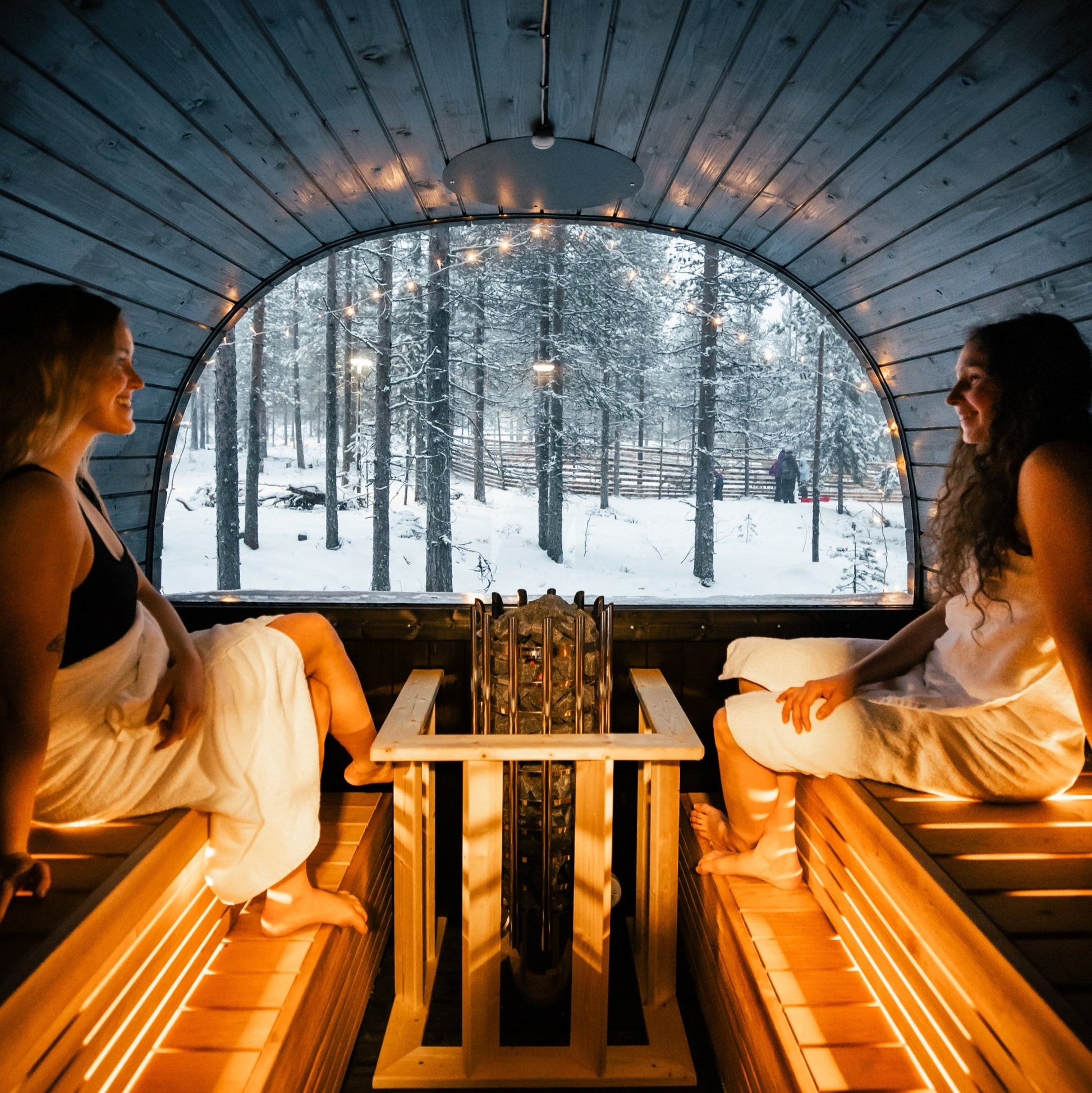 Two women relaxing in a sauna with a snowy forest view at Lapland Winter Park - Snow experiences - vendor