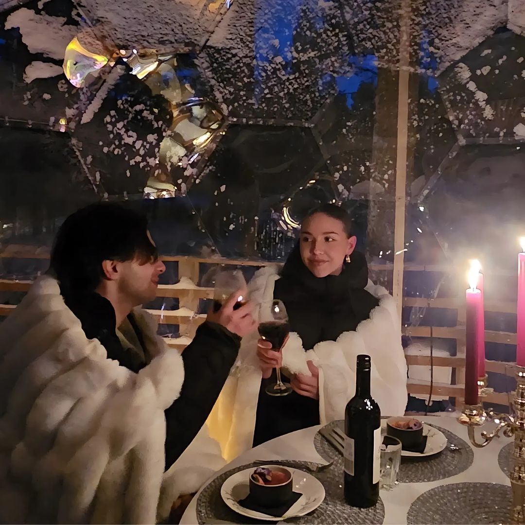 Couple enjoying Luxury dinner in the arctic forest inside a glowing dome with wine and candles Invisible forest lodge