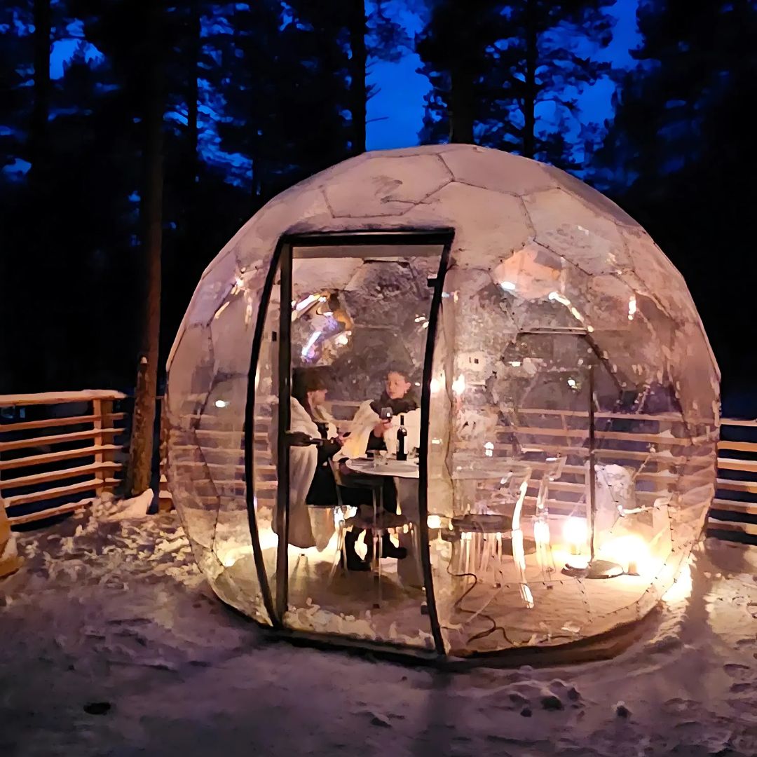 Couple dining inside a glowing dome in the Arctic Forest for Luxury dinner in the arctic forest by Invisible forest lodge