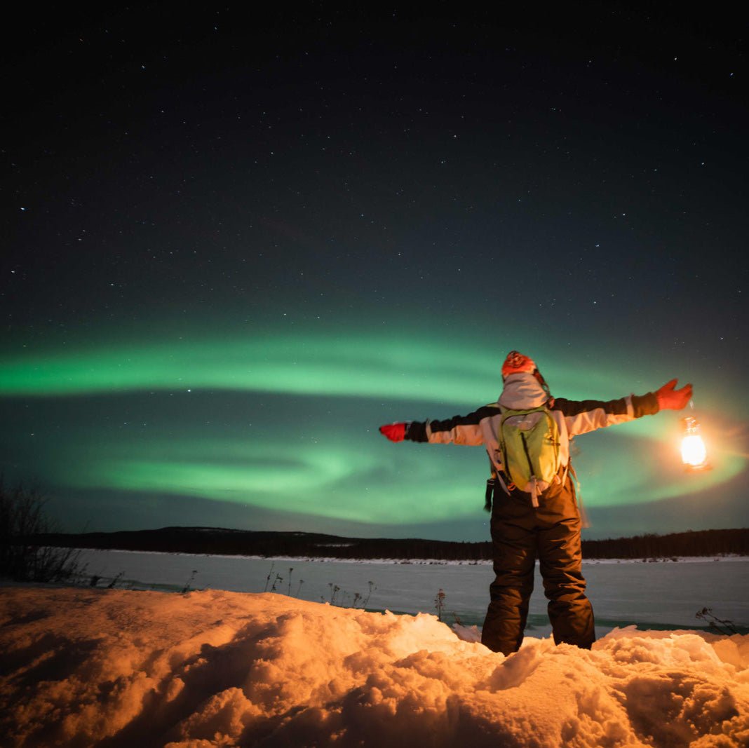Person holding lantern under vibrant Northern Lights during Northern Lights Photography tour by Beyond Arctic