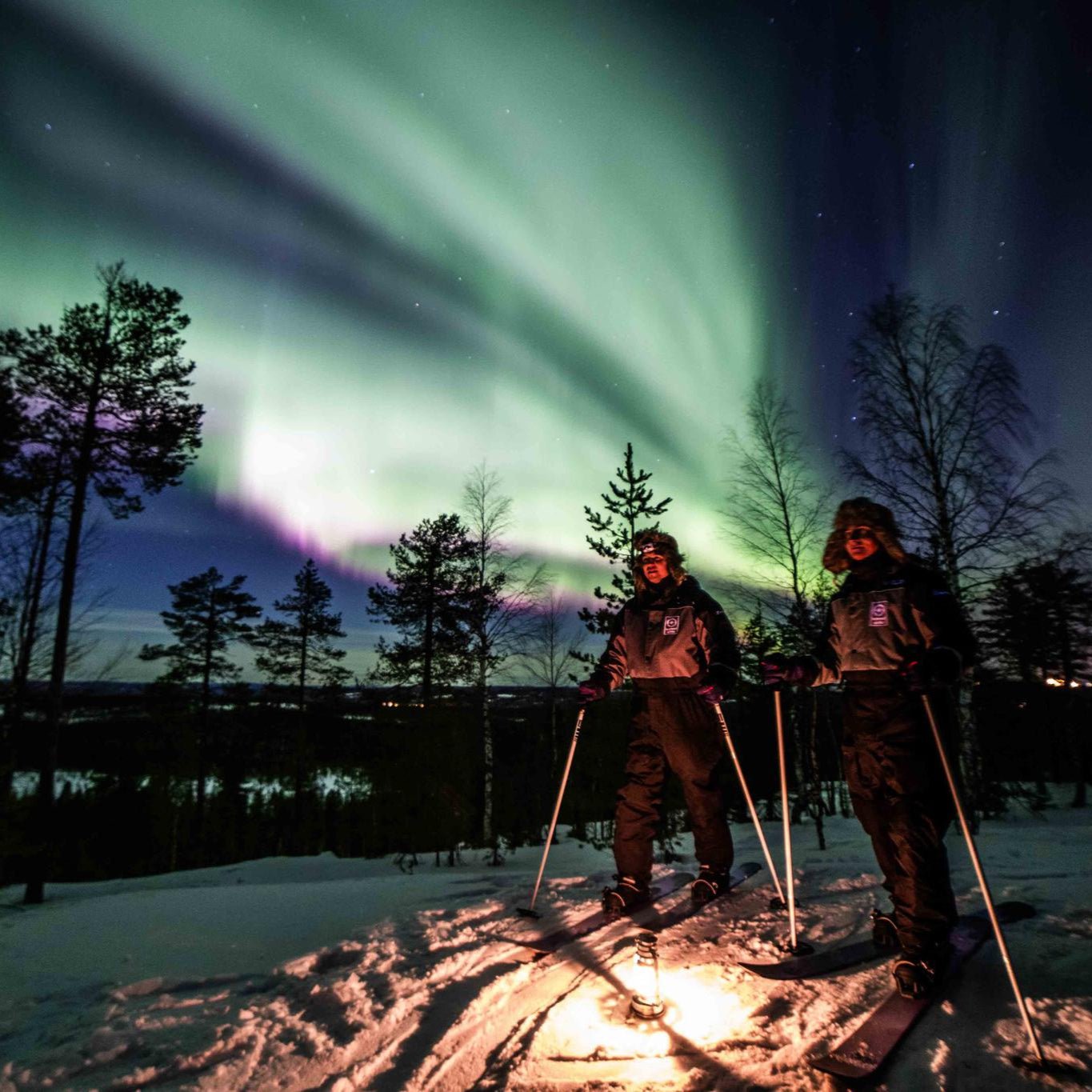Northern Lights skiing adventure night time with skiers under aurora borealis in Arctic forest Beyond Arctic