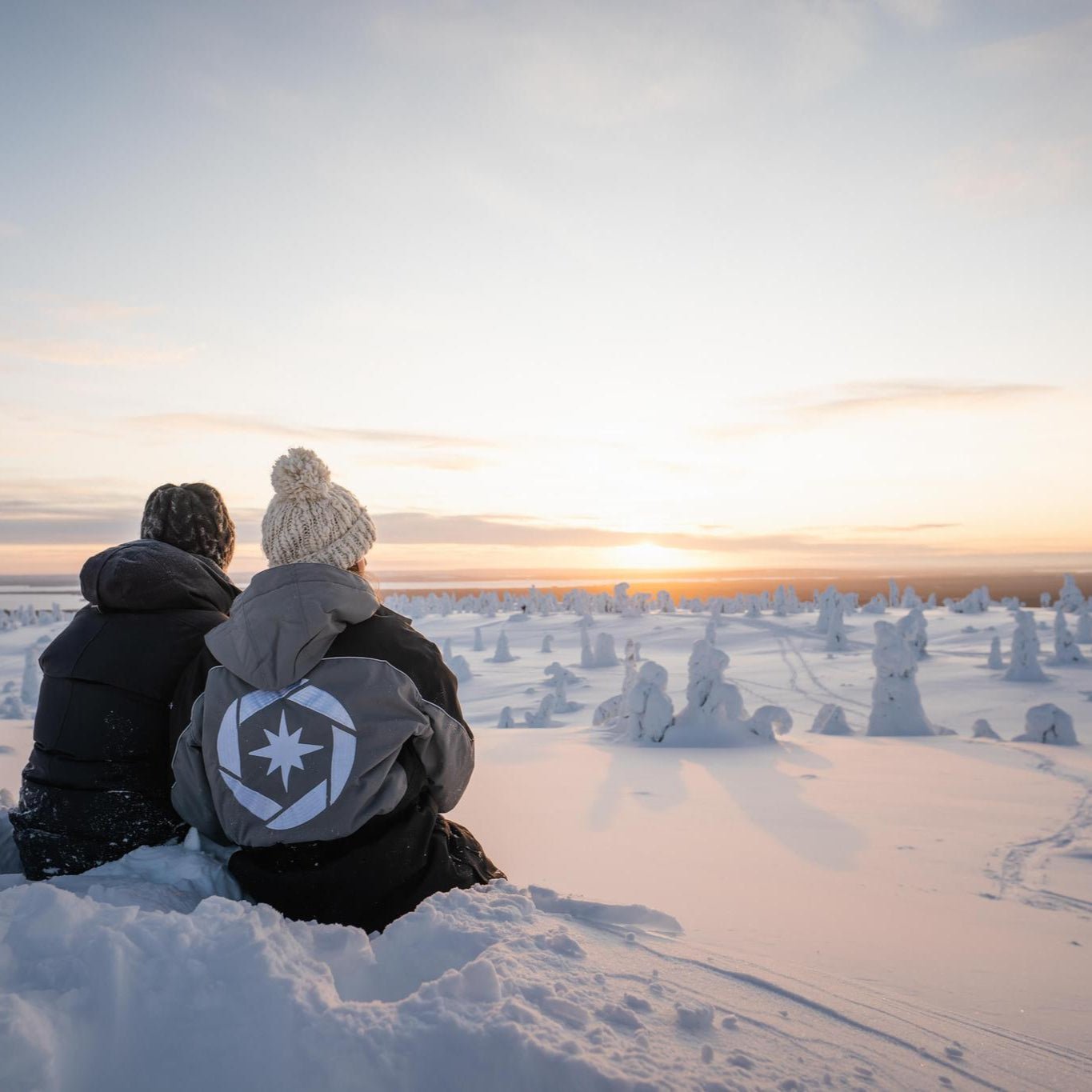 Two people in winter clothing watching a snowy sunset at Riisitunturi wilderness adventure photography tour Beyond Arctic