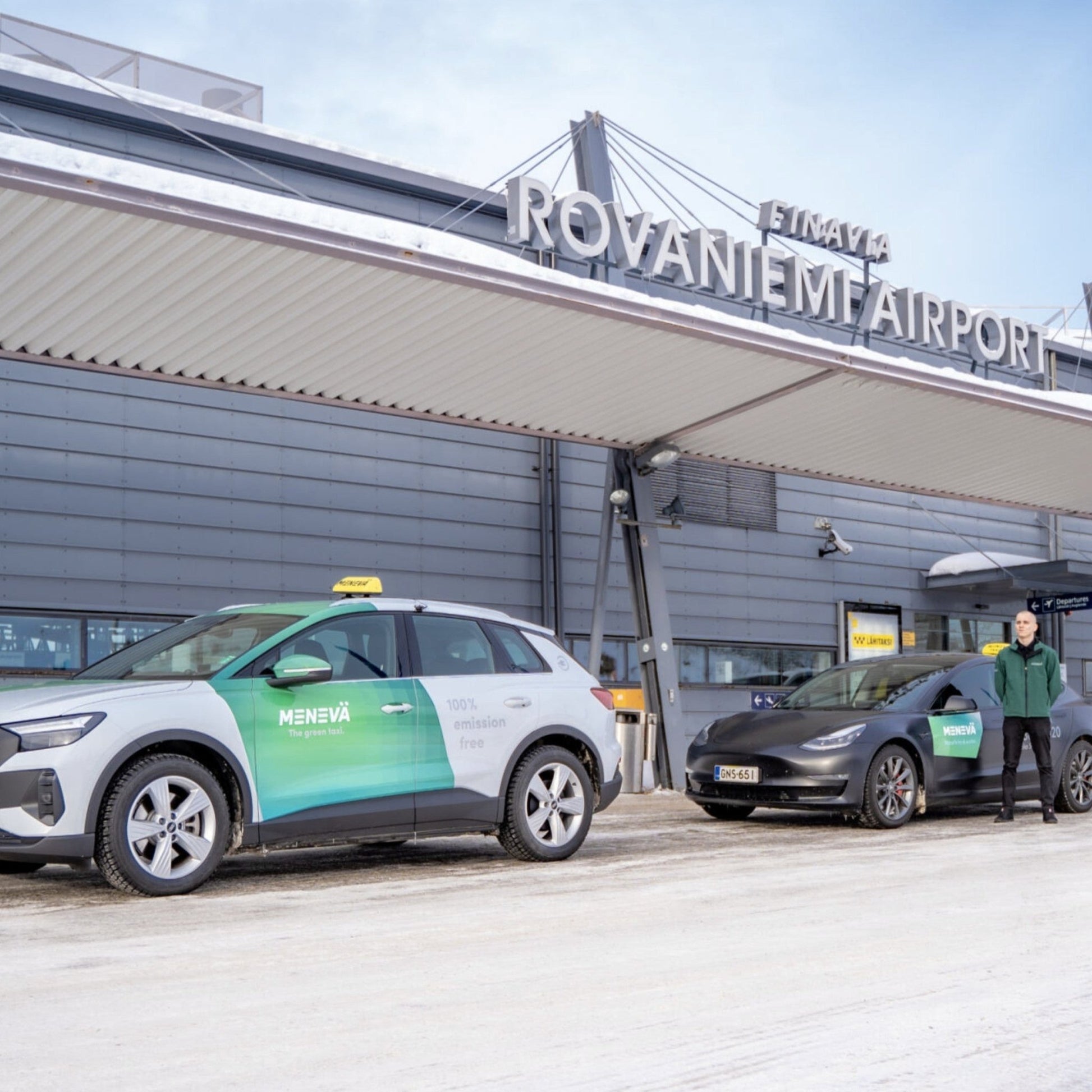 Two electric cars with taxi signs at Rovaniemi Airport in a snowy setting.