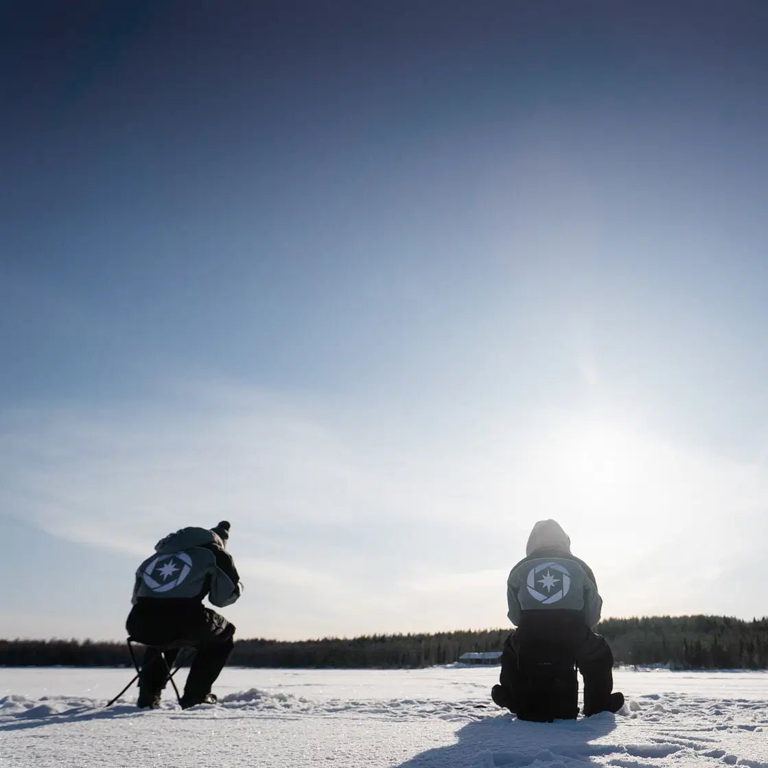 Two people ice fishing on a frozen lake during a Skiing and Fishing on Ice Adventure by Beyond Arctic