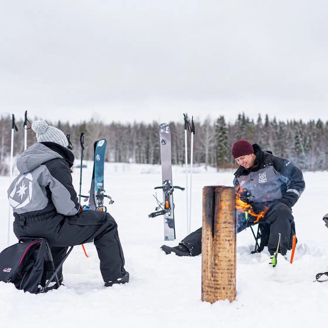 Two people sitting by a fire on snow with skis nearby during Skiing and Fishing on Ice Adventure Beyond Arctic
