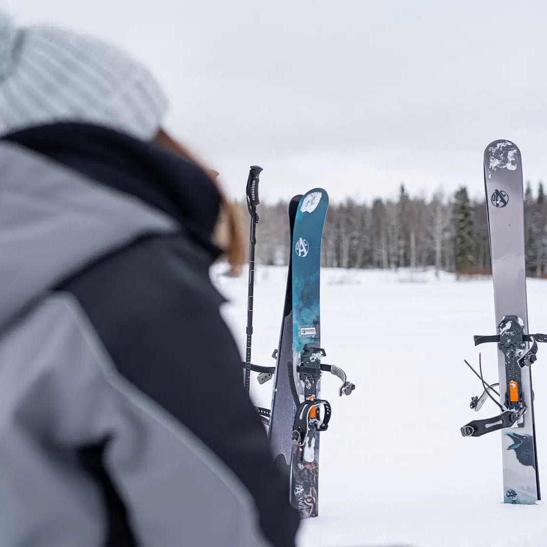 Skis standing upright on snowy lake with skier wearing grey jacket in the background Skiing and Fishing on Ice Adventure