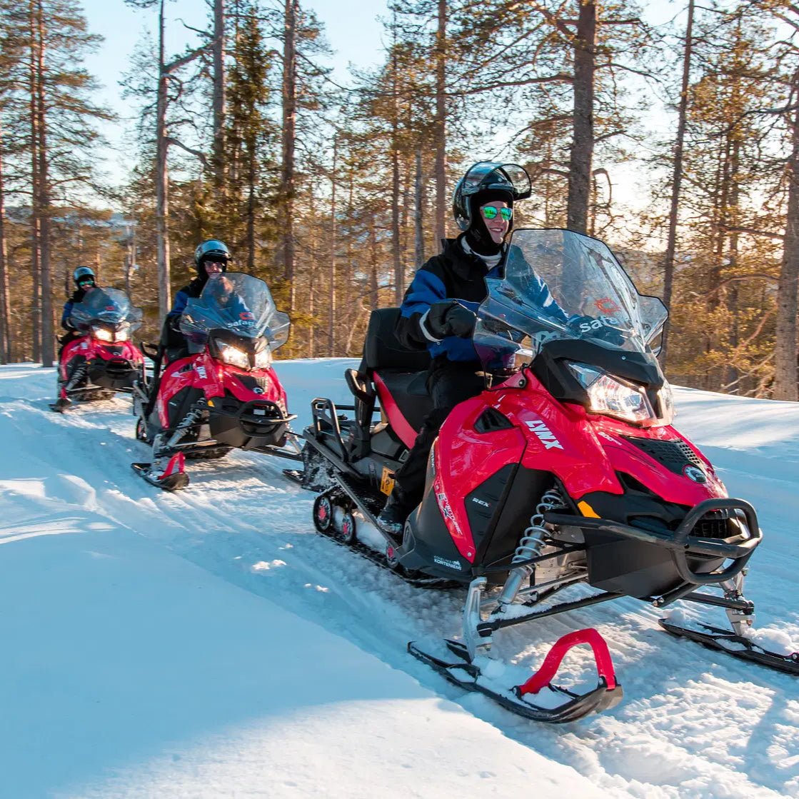 Adults riding red snowmobiles through snowy forest trails during Snowmobile Safari for Adults by Safartica