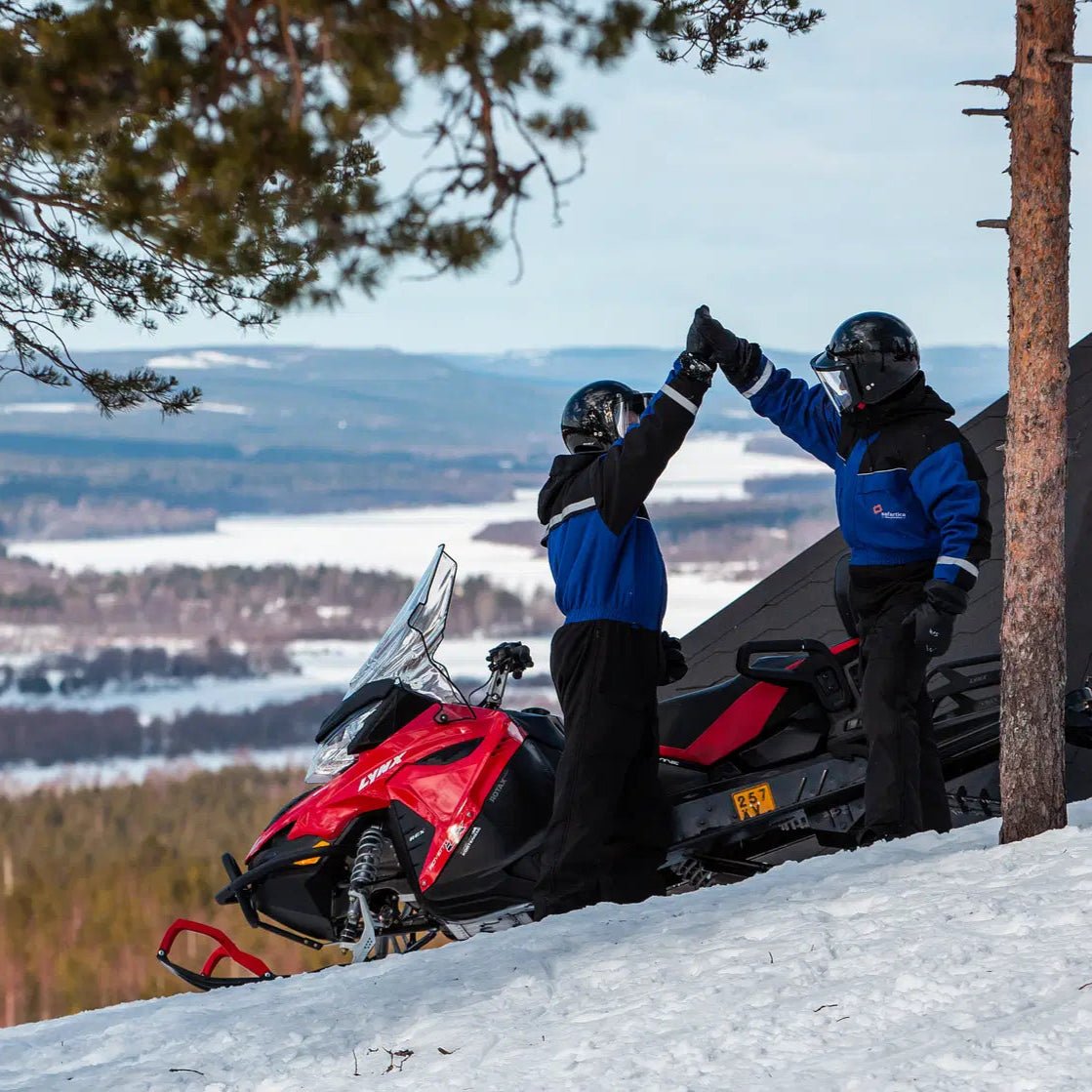 Two adults high-fiving next to a red snowmobile during Snowmobile Safari for Adults by Safartica.