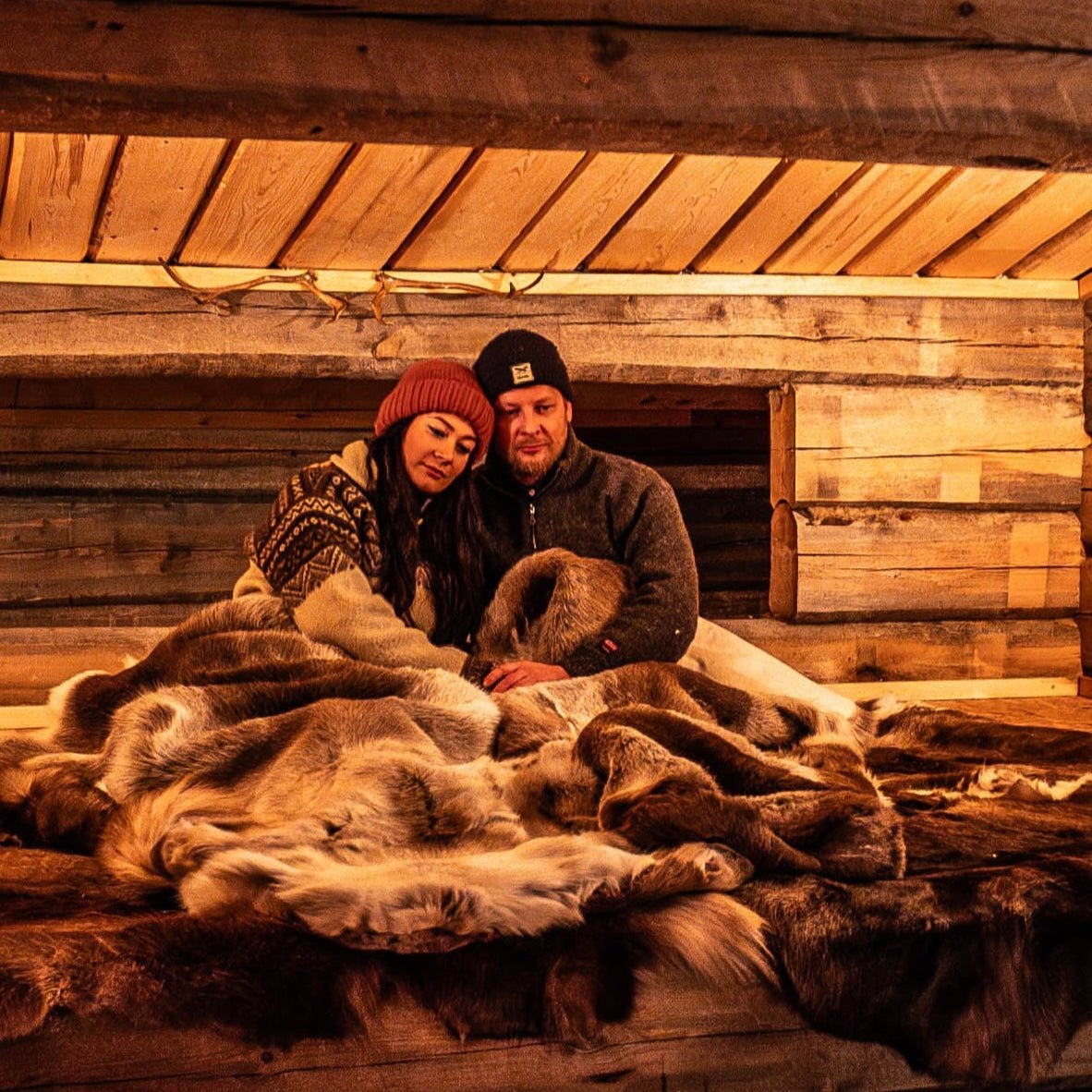 A couple cozy inside a reindeer herder's lean-to with warm reindeer hides, featured in A night in the wilderness.